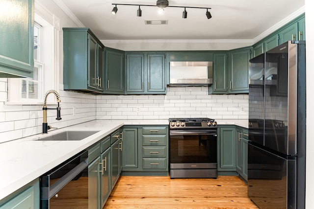 kitchen with ornamental molding, a sink, wall chimney range hood, appliances with stainless steel finishes, and light wood finished floors