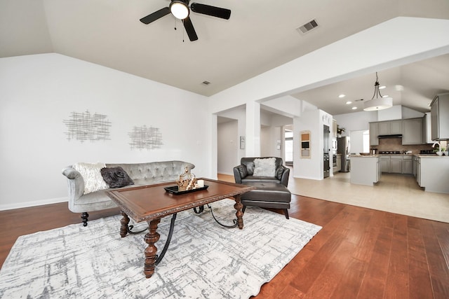 living room with light wood-style floors, lofted ceiling, a ceiling fan, and visible vents