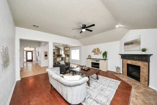 living room with visible vents, a tile fireplace, plenty of natural light, wood finished floors, and vaulted ceiling