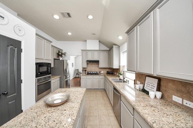 kitchen featuring light stone counters, a sink, stainless steel appliances, under cabinet range hood, and tasteful backsplash