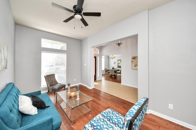 living area with baseboards, wood finished floors, and ceiling fan with notable chandelier