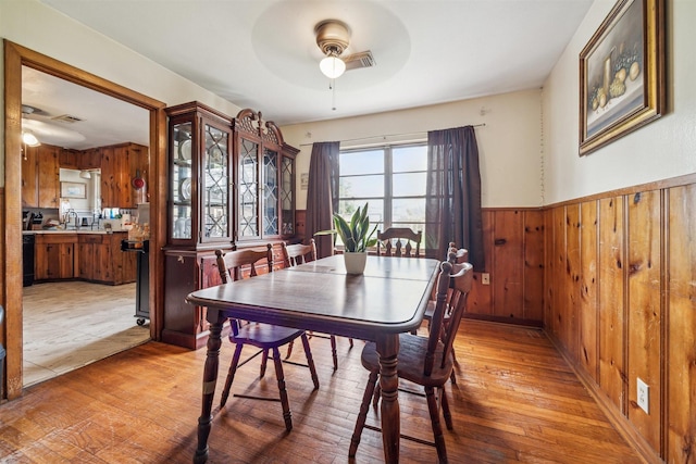 dining space featuring a wainscoted wall, visible vents, light wood-style floors, wooden walls, and ceiling fan