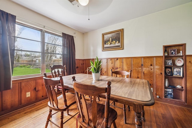 dining area featuring wooden walls, wainscoting, a ceiling fan, and hardwood / wood-style flooring