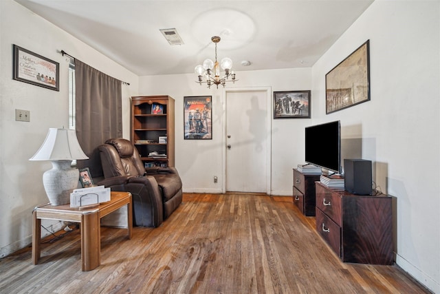 living area featuring a notable chandelier, baseboards, visible vents, and wood finished floors