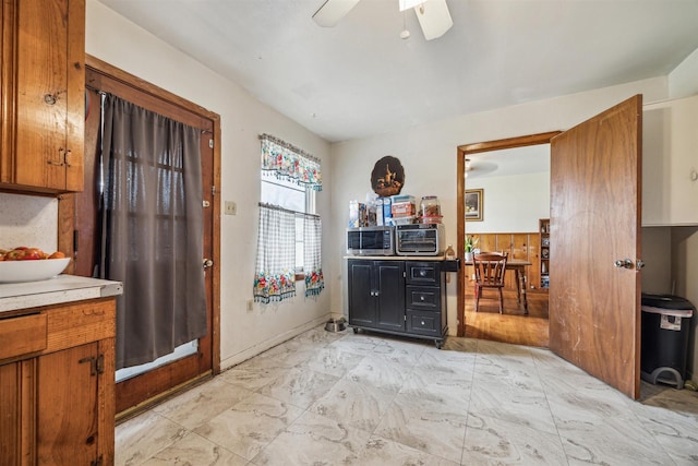 kitchen with light countertops, brown cabinets, marble finish floor, and ceiling fan