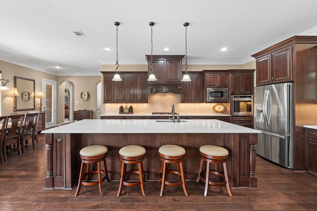 kitchen featuring light countertops, a large island with sink, arched walkways, stainless steel appliances, and a sink