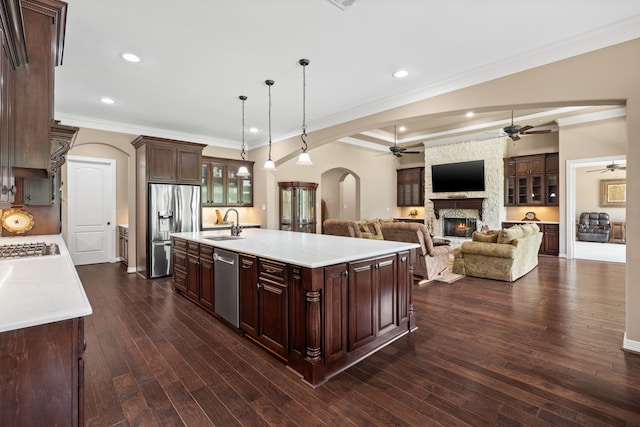 kitchen with a stone fireplace, appliances with stainless steel finishes, arched walkways, a ceiling fan, and a sink