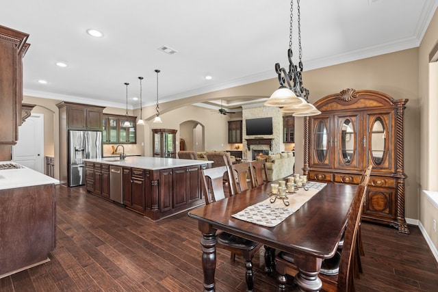 dining room with visible vents, ceiling fan, ornamental molding, a fireplace, and arched walkways