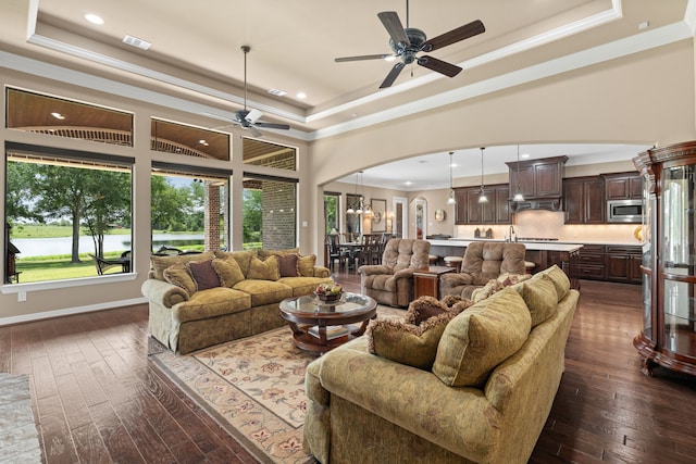 living room featuring visible vents, ceiling fan, arched walkways, a raised ceiling, and dark wood-style flooring