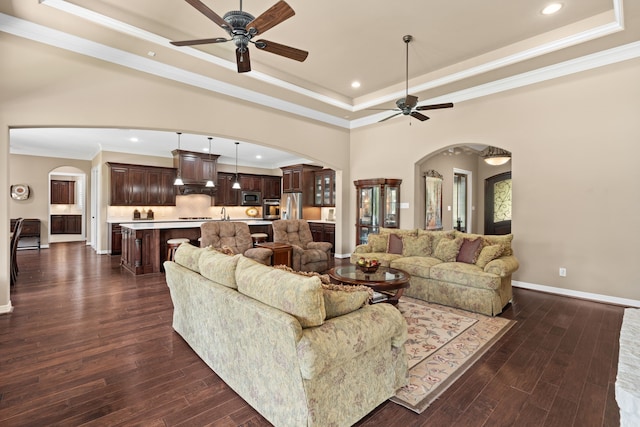 living area featuring dark wood finished floors, a tray ceiling, arched walkways, and ceiling fan