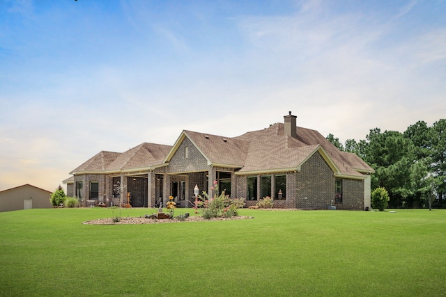 rear view of house with a lawn, a chimney, brick siding, and roof with shingles