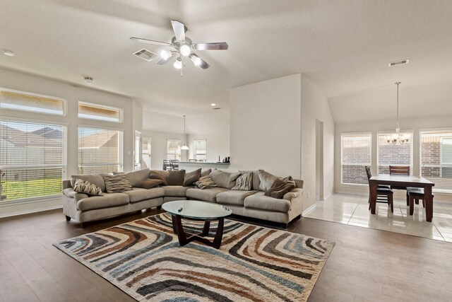 living room featuring a wealth of natural light, visible vents, and ceiling fan with notable chandelier