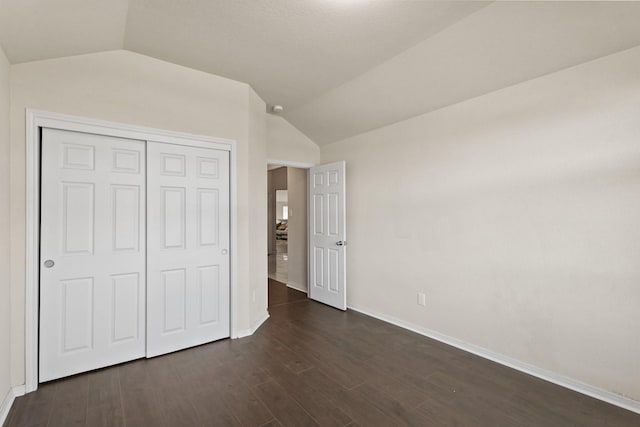 unfurnished bedroom with vaulted ceiling, baseboards, dark wood-style flooring, and a closet