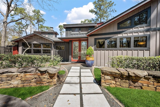 doorway to property with board and batten siding, a chimney, and french doors