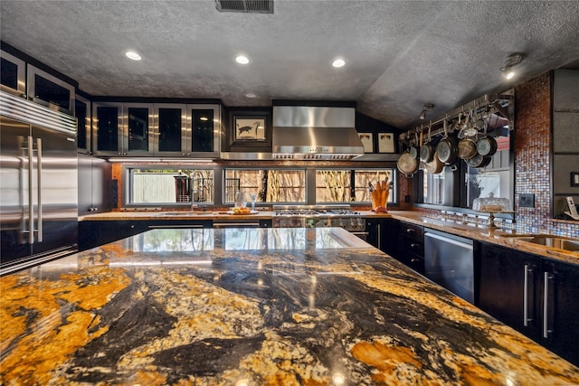 kitchen featuring a sink, stainless steel appliances, a textured ceiling, wall chimney exhaust hood, and dark cabinets