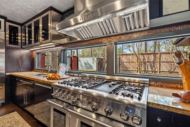 kitchen with dark tile patterned floors, double oven range, a textured ceiling, range hood, and glass insert cabinets