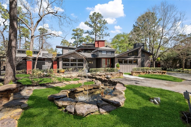 back of property with a small pond, fence, board and batten siding, and a lawn