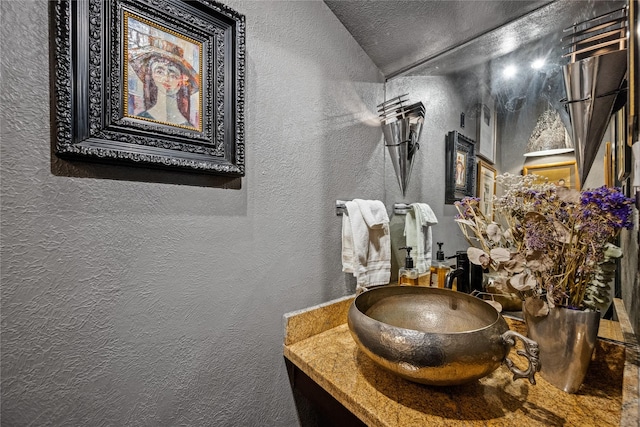 bathroom featuring vaulted ceiling, vanity, and a textured wall