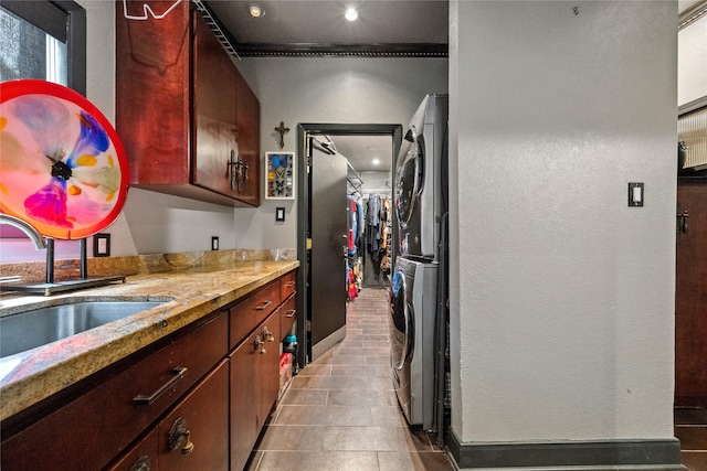 kitchen with crown molding, light stone counters, stacked washing maching and dryer, a textured wall, and a sink