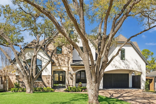 view of front facade with a front yard, stone siding, driveway, and stucco siding