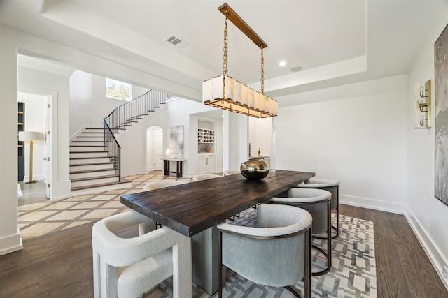 dining area featuring dark wood-type flooring, a tray ceiling, stairway, arched walkways, and baseboards