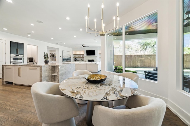 dining area with dark wood-type flooring, baseboards, recessed lighting, a fireplace, and ceiling fan with notable chandelier