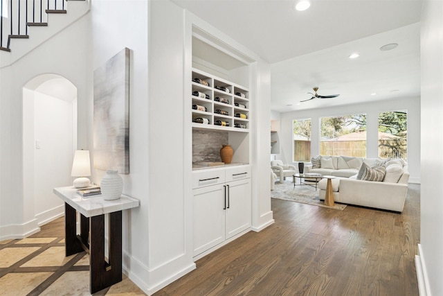 hallway with built in shelves, baseboards, dark wood finished floors, recessed lighting, and arched walkways