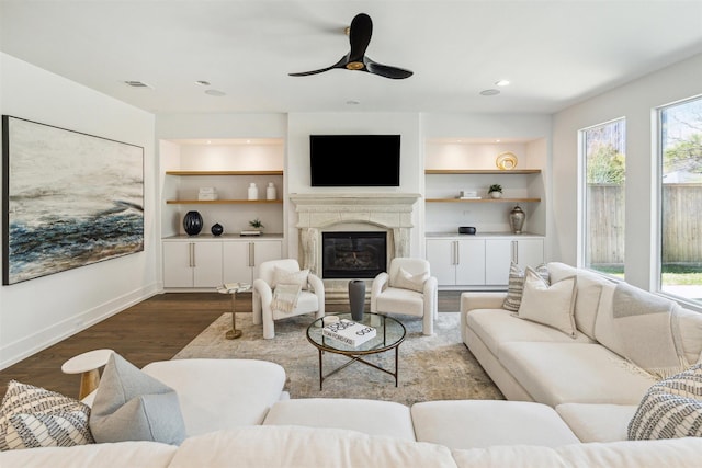 living area featuring built in shelves, a ceiling fan, wood finished floors, visible vents, and baseboards