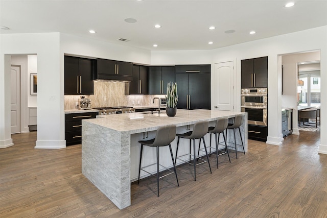 kitchen with a sink, backsplash, wood finished floors, built in fridge, and stainless steel double oven