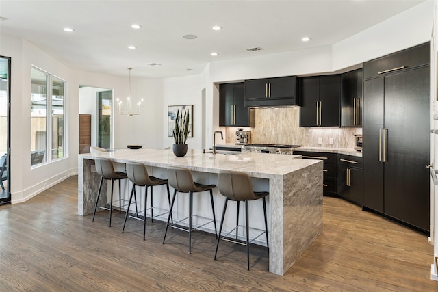 kitchen featuring dark cabinetry, a spacious island, a sink, built in refrigerator, and range