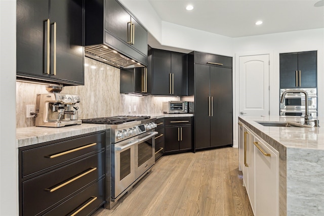 kitchen with high quality appliances, light stone counters, decorative backsplash, light wood-style flooring, and dark cabinets