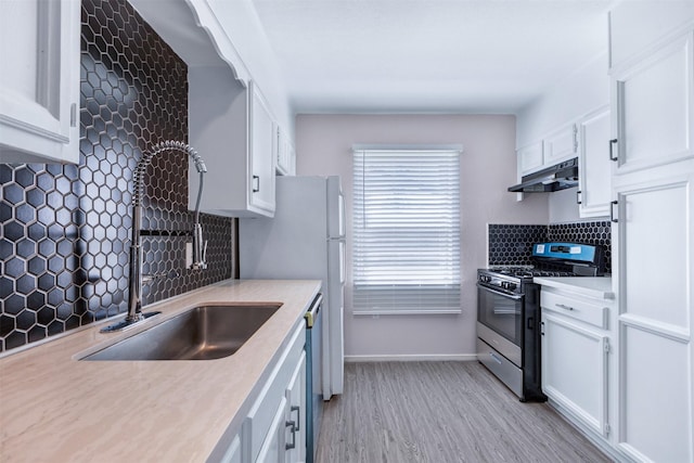 kitchen featuring under cabinet range hood, light countertops, white cabinets, stainless steel gas range, and a sink