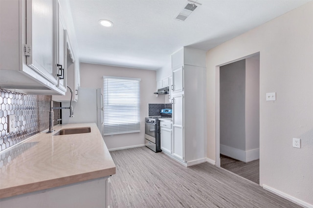 kitchen with visible vents, stainless steel gas stove, a sink, under cabinet range hood, and light countertops