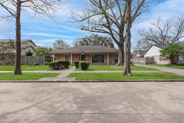 view of front of home featuring a front lawn, fence, concrete driveway, brick siding, and a chimney