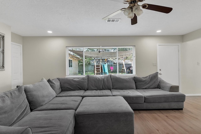 living area featuring a textured ceiling, wood finished floors, visible vents, and ceiling fan