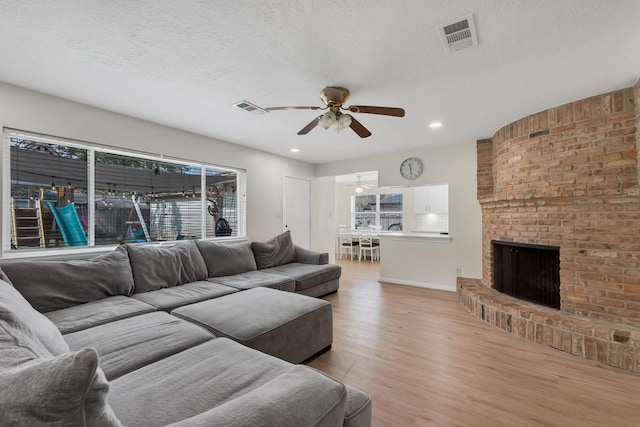 living area featuring visible vents, light wood-style floors, a ceiling fan, and a textured ceiling