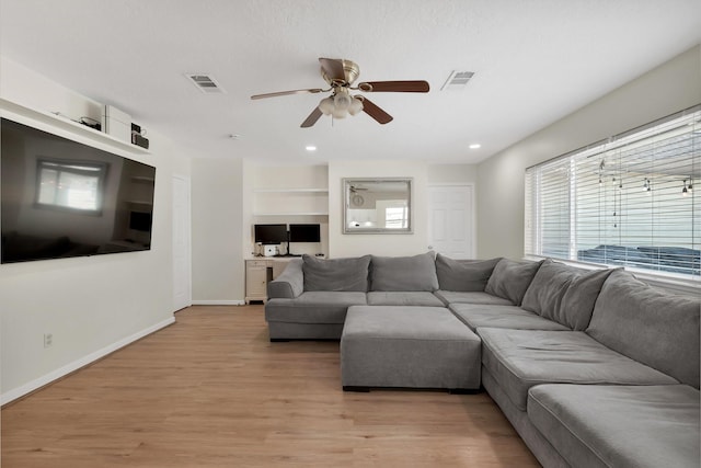 living room featuring visible vents, baseboards, ceiling fan, and light wood-style flooring