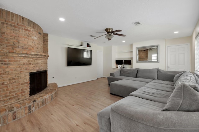 living room with a fireplace, visible vents, light wood finished floors, and ceiling fan