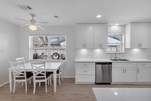 kitchen featuring visible vents, a sink, stainless steel dishwasher, backsplash, and light wood-style floors