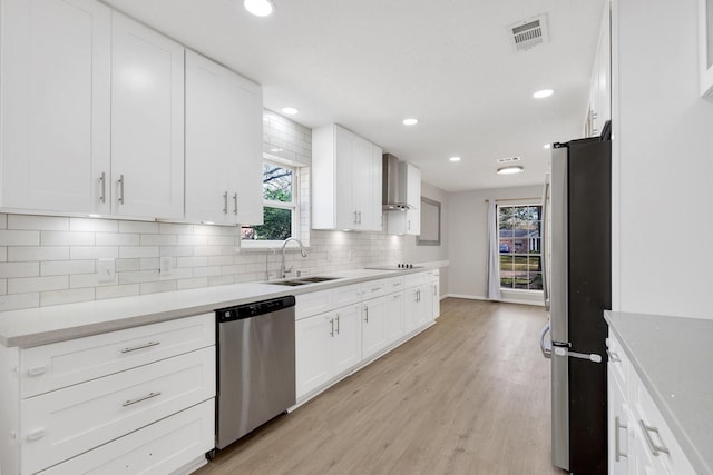 kitchen featuring visible vents, wall chimney range hood, light wood-type flooring, stainless steel appliances, and a sink