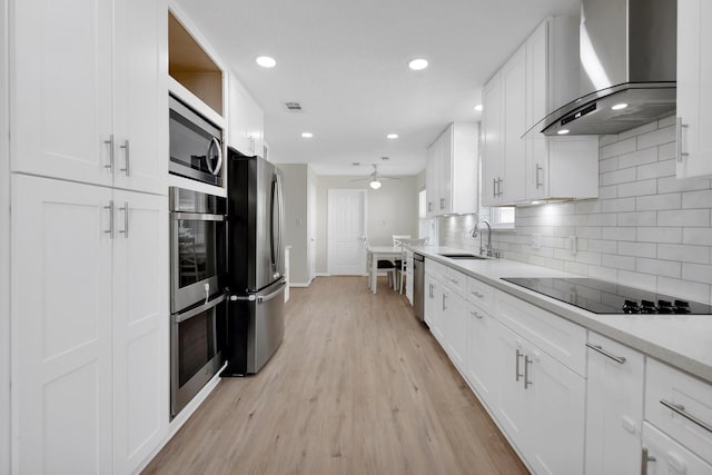 kitchen featuring visible vents, a sink, appliances with stainless steel finishes, white cabinetry, and wall chimney range hood