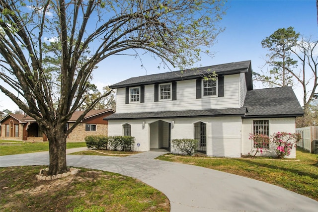 view of front of house featuring brick siding, curved driveway, a front lawn, and a shingled roof