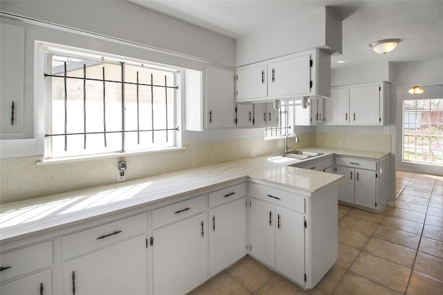 kitchen with light countertops, light tile patterned floors, a peninsula, white cabinetry, and a sink