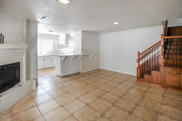 living area featuring visible vents, a textured ceiling, baseboards, a brick fireplace, and stairs