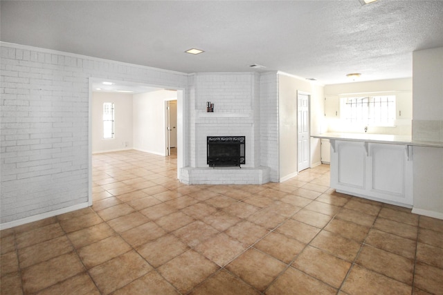 unfurnished living room featuring baseboards, brick wall, ornamental molding, a textured ceiling, and a brick fireplace