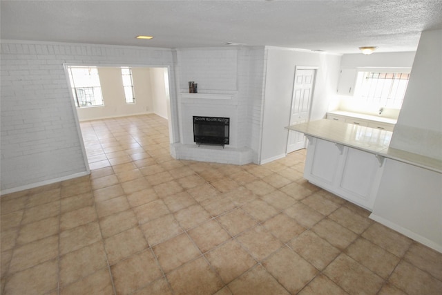 unfurnished living room featuring brick wall, a brick fireplace, baseboards, heating unit, and a textured ceiling