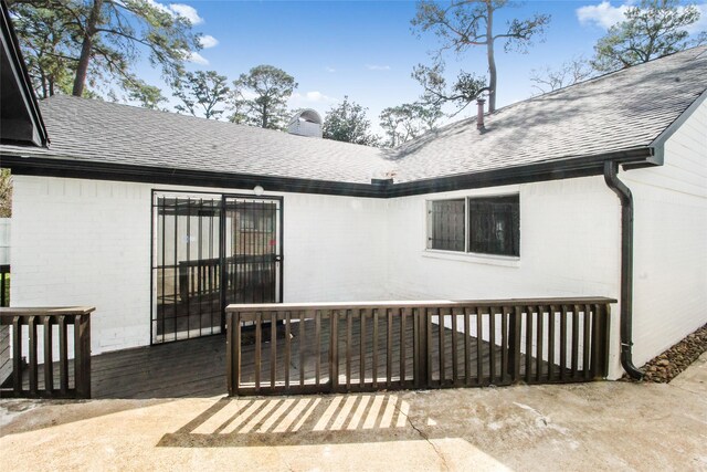 property entrance with a deck, brick siding, roof with shingles, and a chimney