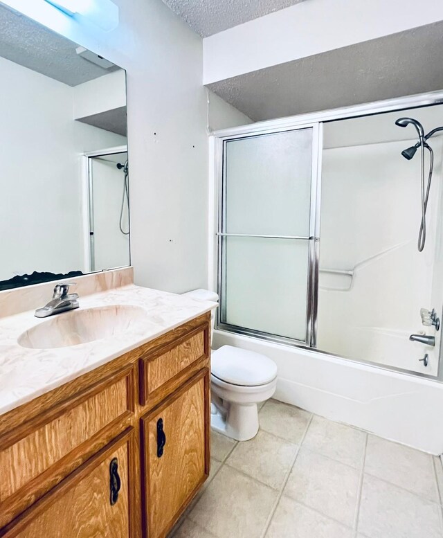 full bathroom with tile patterned flooring, bath / shower combo with glass door, toilet, vanity, and a textured ceiling