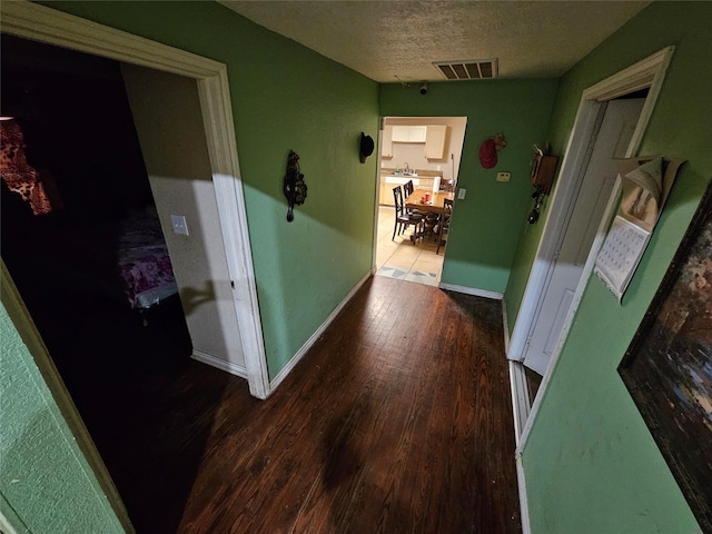 hallway with visible vents, a textured ceiling, baseboards, and wood finished floors