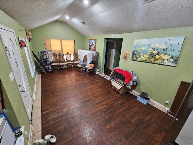 interior space featuring a textured ceiling, hardwood / wood-style flooring, a textured wall, and vaulted ceiling